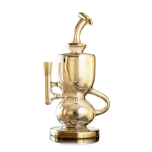 The MJ Arsenal Titan Mini Dab Rig features gold-tinted borosilicate glass, a curved neck, side mouthpiece, and intricate chamber design on a stable round base for an elevated smoking experience.