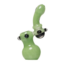 The Human Grade Sherlock Bubbler is a handmade green borosilicate glass pipe with an abstract, rounded shape, glossy finish, and black accents on the sides and mouthpiece, shown against a white background.