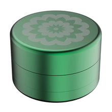 The Flower Mill 2.5" Next Gen Standard Grinder is a round, green aircraft-grade aluminum container featuring an engraved floral mandala design on the lid, displayed against a white background—a true Flower Mill original.