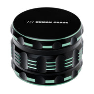 The Human Grade Grinder 5T (2.5") is a black, cylindrical 4-piece aluminum grinder with light green accents, grooves, and "HUMAN GRADE" printed in white on the top.