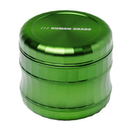 The Human Grade Grinder 6M (2.5") is a metallic green aluminum herb grinder with ribbed sides, "HUMAN GRADE" on the lid, and an ergonomic design for comfort.