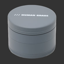 The Human Grade Grinder 4R (2.5") is a gray, round, metal 4-piece grinder with "HUMAN GRADE" in white on the lid and textured edges for grip.