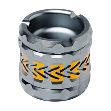 The Human Grade Grinder 8AT is a metallic cylindrical aluminum grinder with a grooved surface and black-and-orange zigzag design, featuring a recessed circular top with notched edges—ideal for use as a 4-piece grinder.
