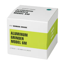 A white and green box labeled Human Grade Grinder 6M (2.5") displays black text, product details, and showcases this ergonomic 4-piece, 63 mm aluminum herb grinder.