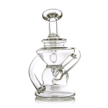 The MJ Arsenal Hydra Mini Dab Rig, a clear glass piece with a cylindrical base, curved handles, and a tall rounded stopper, features an intricate artistic design and is photographed against a white background.