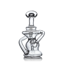 The MJ Arsenal Hydra Vape Edition is a clear glass sculpture with abstract curves and a round, flat-topped stopper, resembling a mini dab rig on a reflective white background.