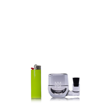The MJ Arsenal ISO Station, a compact, transparent borosilicate glass accessory with a black insert, is displayed next to a bright green lighter on a white background.