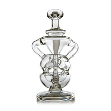 The MJ Arsenal Infinity Mini Dab Rig features a clear glass body with an intricate, abstract design similar to a fab egg percolator, curved handles, an upright round base, and a matching glass stopper.