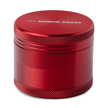 The Human Grade Grinder 1A (2" 4-Piece) is a metallic red, cylindrical grinder with a textured grip and "HUMAN GRADE" printed in white on the top lid.