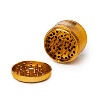 The Human Grade Grinder 6M (2.5") in gold is shown with its lid off, revealing sharp grinding teeth inside. Its ergonomic design stands out against a white background.