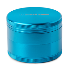 The Human Grade Grinder 1B (2.5") is a metallic blue aluminum grinder with textured edges, a pollen screen, and "HUMAN GRADE" engraved on the top lid.