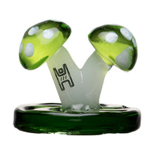 The Mushroom Carb Cap is a borosilicate glass sculpture with two green mushrooms with white spots on a dark green base and black abstract symbols on the stems—an eye-catching dab rig accessory against a white background.