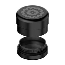 A black, round Flower Mill 2" Next Gen Premium Grinder features a floral lid design and opens to show its 2" mill plates and mesh filter compartments.