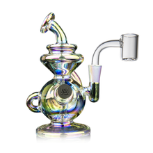 The MJ Arsenal Mini Jig Mini Dab Rig is a colorful, iridescent concentrate rig with a round base, curved neck, side handle, built-in storage jar, and a clear glass bowl attachment, displayed against a white background.