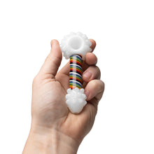 A hand holds the Human Grade Rainbow Spoon Pipe, featuring a white bowl and end with textured bumps, plus a rainbow-striped stem. Crafted from durable borosilicate glass, it's shown against a plain white background.