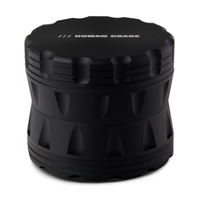 The Human Grade Grinder 2A (2.5" 4-Piece) is a matte black, cylindrical aluminum grinder with ridged sides and "HUMAN GRADE" in white on the lid. It features a sleek, industrial look and includes a built-in pollen screen for easy use.