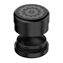 The Flower Mill 2.5" Next Gen Premium Grinder is a black, round grinder with an engraved floral pattern on the lid, pictured slightly open to display its inner grinding compartment, mesh screen, and precision mill plates.
