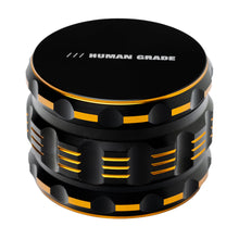 A black and orange 4-piece Human Grade Grinder 5T (2.5") made of aluminum, featuring textured grooves and "HUMAN GRADE" printed in white on the top lid.