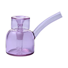 The NWTN Home Vesper Bubbler is a transparent purple borosilicate glass piece with a short round base, built-in downstem, 14mm slide, and angled spout, shown on a white background.