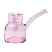 The NWTN Home Vesper Bubbler is a compact, transparent pink piece crafted from durable borosilicate glass, featuring a curved spout, cylindrical base, short neck, built-in downstem, and 14mm slide compatibility for smooth sessions.