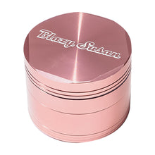 The Blazy Susan Grinder V2 is a shiny, pink, cylindrical aluminum grinder featuring a spacious grind chamber and "Blazy Susan" engraved in white script on the top.