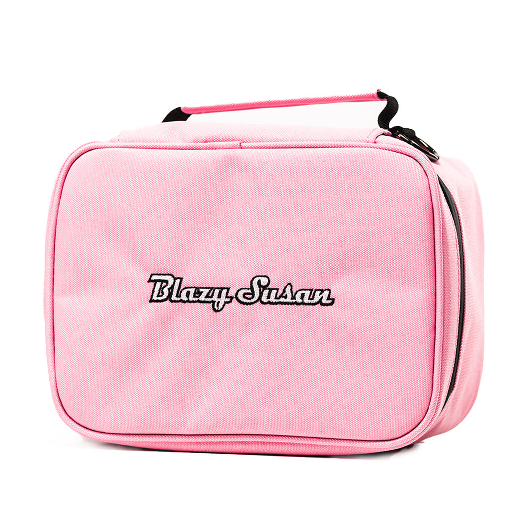 The Blazy Susan Stash Bag is a light pink, rectangular bag with a black zipper, front embroidered logo, top handle, and rolling tray compatibility for stylish, organized storage.