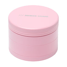 The Human Grade Grinder 4C (2.5”) is a round, pink aluminum herb grinder featuring a screw-top lid with textured edges and "HUMAN GRADE" embossed on the lid in a simple font.
