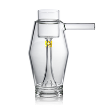 Set against a white background, the MJ Arsenal Proxy Bubbler features clear borosilicate glass with an angular body, a right-side cylindrical spout, and a yellow geometric logo on the front.
