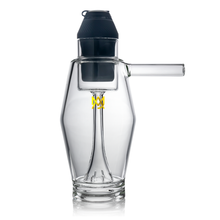 The MJ Arsenal Proxy Bubbler is a clear borosilicate glass dabbing accessory with a cylindrical body, side handle, black top, yellow logo on the front, and an interior vertical glass tube.