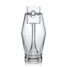 The MJ Arsenal Proxy Bubbler features a clear, modern borosilicate glass build with angular sides, a smooth cylindrical neck, and a unique circular handle near the top. Its sleek, minimalistic design emphasizes transparency and symmetry.