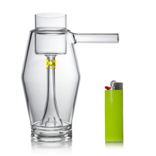 The MJ Arsenal Proxy Bubbler, a clear borosilicate glass water pipe with a side handle, is displayed beside a bright green lighter on a white background.