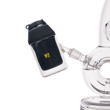 A close-up of MJ Arsenal Proxy Attachments—a clear borosilicate glass water pipe with a black electronic vaporizer (gold crown logo), set at an angle. Compatible with MJ Arsenal products. White background.