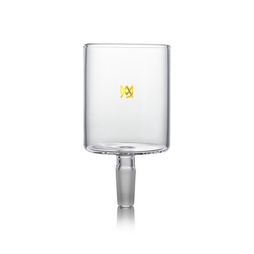 A clear borosilicate glass cup with a cylindrical shape, short stem, and small gold logo on the front sits on a white background. Designed for versatile use, it is compatible with MJ Arsenal Proxy Attachments.