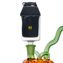A close-up of MJ Arsenal Proxy Attachments—a black and clear vaping accessory with a yellow logo, connected to a green borosilicate glass piece on an amber base, isolated on a white background.