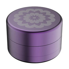 The Flower Mill 2.5" Next Gen Standard Grinder is a round, metallic, purple container made from aircraft-grade aluminum with a silver engraved floral mandala design on the lid, shown against a white background.