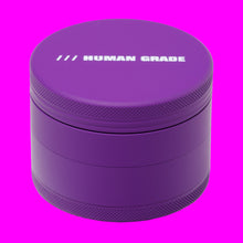 The Human Grade Grinder 4R (2.5") is a round, purple 4-piece grinder with textured edges, "HUMAN GRADE" printed in white on the lid, and a built-in pollen catcher for added convenience.