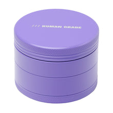 The Human Grade Grinder 4C (2.5") is a round, purple aluminum 4-piece herb grinder with textured edges and "HUMAN GRADE" printed in white on the lid—sturdy and ideal for keeping contents fresh and secure.