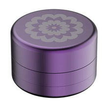 The Flower Mill 2" Next Gen Standard Grinder is a small, round, purple metal herb grinder featuring a decorative light floral mandala design on the lid, displayed against a white background.