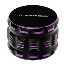 The Human Grade Grinder 5T (2.5") is a black cylindrical aluminum grinder with ridged sides, purple accents, and "HUMAN GRADE" on the top lid, offering efficient grinding in a sleek design.