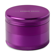 The Human Grade Grinder 1B (2.5") is a metallic purple aluminum grinder with textured edges, "HUMAN GRADE" engraved on the lid, and features a pollen screen inside.