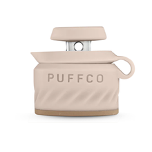The Puffco Peak Pro Joystick Cap is a beige silicone accessory with "PUFFCO" embossed, a loop handle, a metallic top piece, and provides directional airflow like a joystick carb cap; photographed on a white background.