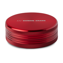 The Human Grade Grinder 1C (2.5" 2-Piece) is a round, metallic red aluminum grinder with textured sides and "HUMAN GRADE" printed in silver on the top.