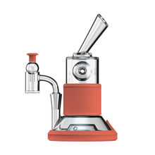 The Softglass Tandem Rig Kit is a modern dab rig featuring a slanted mouthpiece, made from borosilicate glass and platinum-cured silicone with red silicone accents on the base and middle. A small red-capped glass piece is attached on the left, set on white.