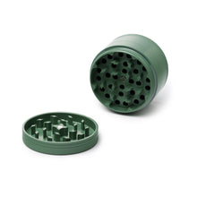 The Human Grade Grinder 4C (2.5") is a green, two-piece aluminum herb grinder with a cylindrical shape, shown opened with both parts side by side and interlocking teeth visible inside each section.