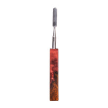 The MJ Arsenal Stabwood Dab Tool features a stainless steel flat blade and a resin handle with red and brown woodgrain patterns, displayed against a white background.