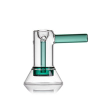 The MJ Arsenal Cove Glass Bubbler, made from clear borosilicate glass with a green handle and inner tube, features a wide conical base and cylindrical chamber, all set against a white background.