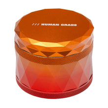 The Human Grade Grinder 7F (2.5") is a shiny, faceted orange aluminum herb grinder with "HUMAN GRADE" in white on top, shown against a white background.