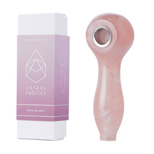 A Gemstone Spoon Pipe with a rose quartz gemstone bowl sits next to its pink and white rectangular box labeled Astral Project Rose Quartz.