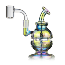 The MJ Arsenal Royale Mini Dab Rig has an iridescent finish, round base, curved neck, external glass details, and a fab egg perc for smooth hits. Made from durable borosilicate glass with rainbow hues and a stylized logo on the front.
