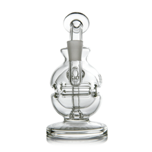 The MJ Arsenal Royale Mini Dab Rig is a clear borosilicate glass water pipe featuring a round base, curved neck, central chamber with intricate glasswork, fab egg percolator, and accessory joint.